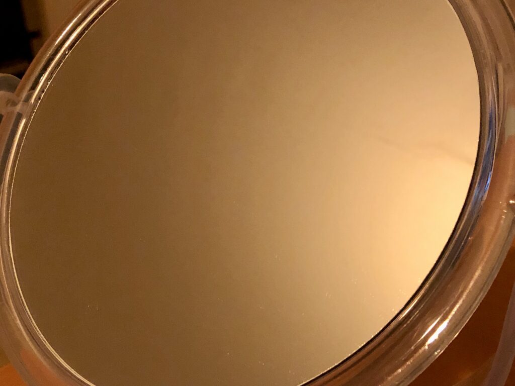Close-up of a circular bathroom mirror, reflecting only a featureless ceiling